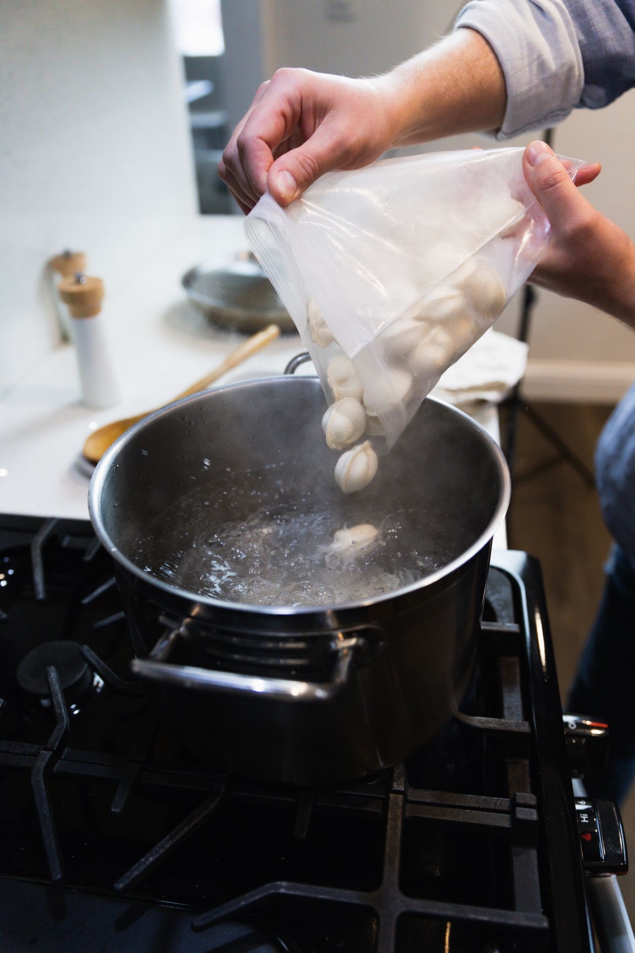 A person adding dumplings from a plastic bag into a pot of boiling water on a stove. A person adding dumplings from a plastic bag into a pot of boiling water on a stove.